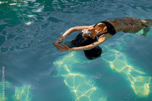 Brunette caucasian model in bikini floating in the pool water