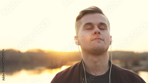 Young handsome man with closed eyes listens to music on beach during sunset.