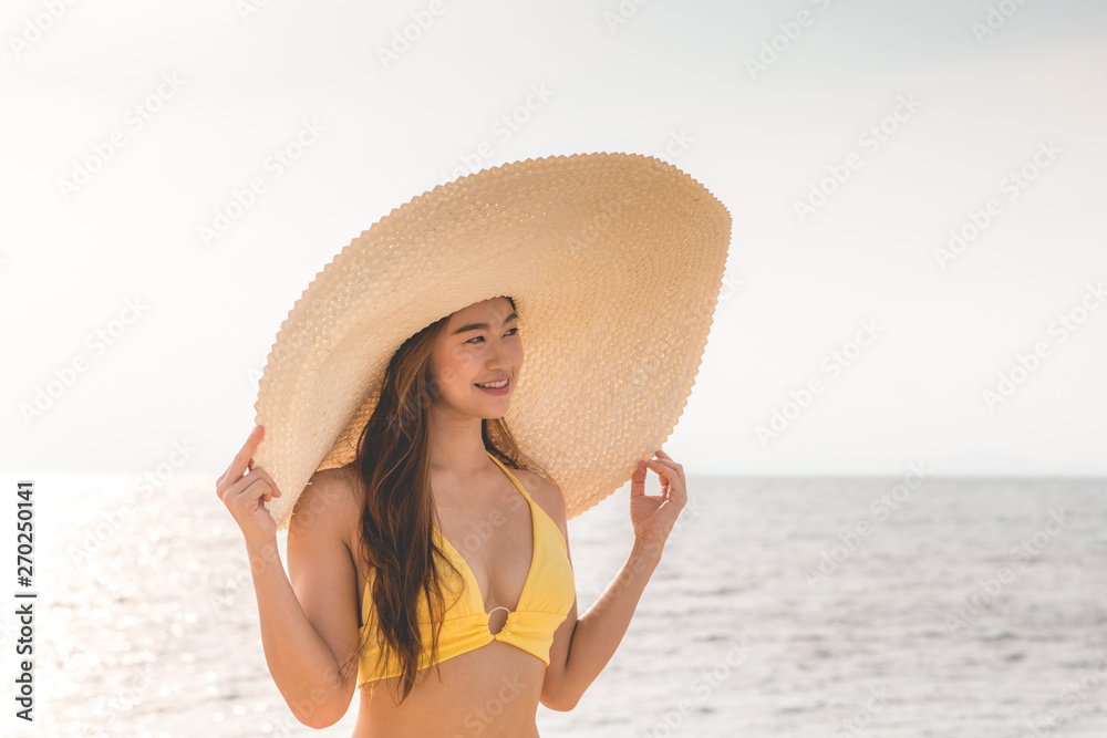 Attractive Asian young woman wearing yellow bikini smile enjoy with summer vacation on the beach feeling so happiness and cheerful,Travel in tropical beach in Thailand,vacations and relaxation Concept