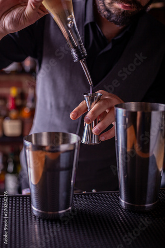 barman preparing cocktai and pours liquid into the jigger in a cocktail bar