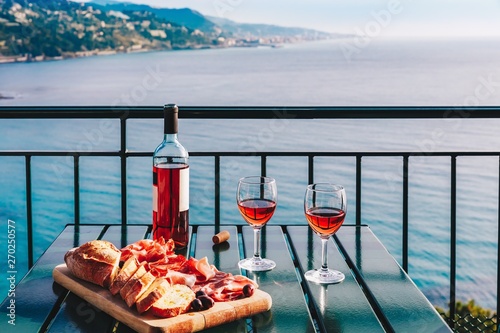 Fototapeta Naklejka Na Ścianę i Meble -  Two glasses of wine and italian snacks  with amazing view at sunset in Italy.