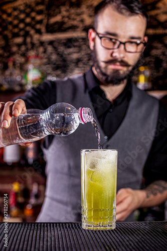 Bartender pouring a cocktail from the steel shaker on the bar counter on the blurred background photo