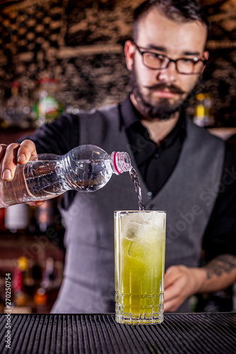 Bartender pouring a cocktail from the steel shaker on the bar counter on the blurred background