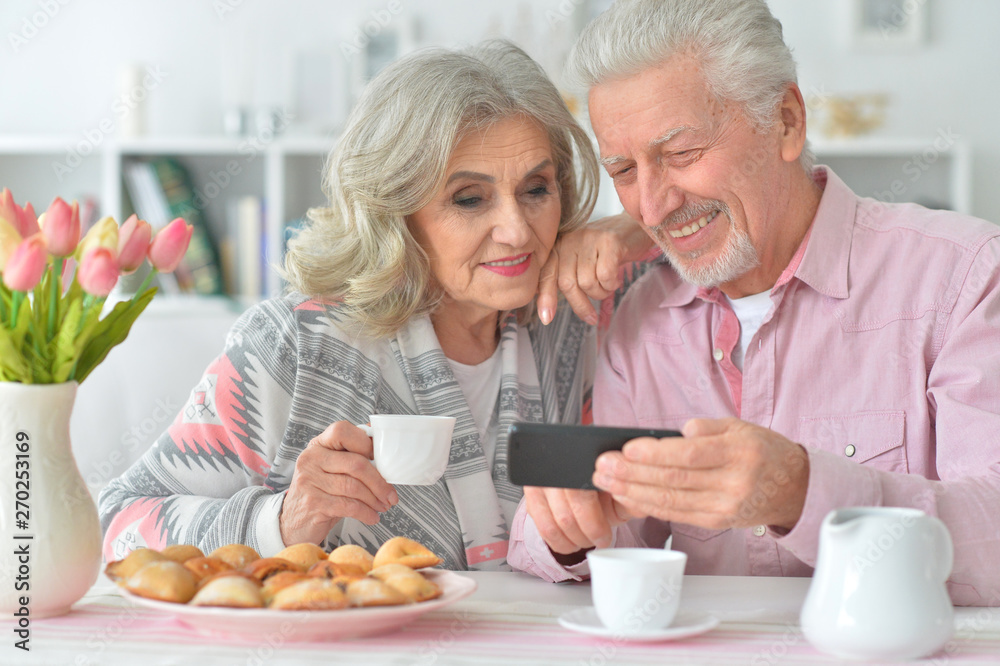 Portrait of happy senior couple with smartphone drinking tea