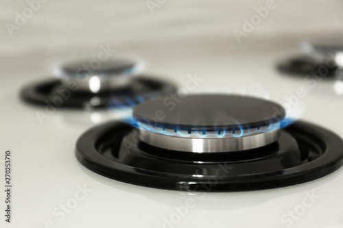 Gas burner with blue flame on modern stove, closeup