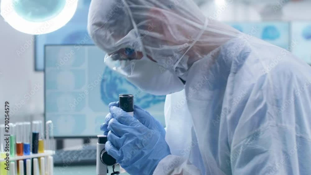 Scientist in coverall presents a sample then puts it under the microscope for inspection. Research and science Scientist in coverall presents a sample then puts it under the microscope for inspection. Research and science