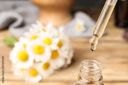 Pipette with essential oil over bottle on blurred background, closeup. Space for text