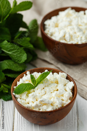 fresh homemade cottage cheese in a wood bowl with mint leaves, on white background. top view