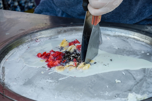 The process of making asian stir fried roll ice cream from fruit and cream in an ice pan with spatulas. Blurred motion hands and spatulas when cooking. Selective focus - Изображение