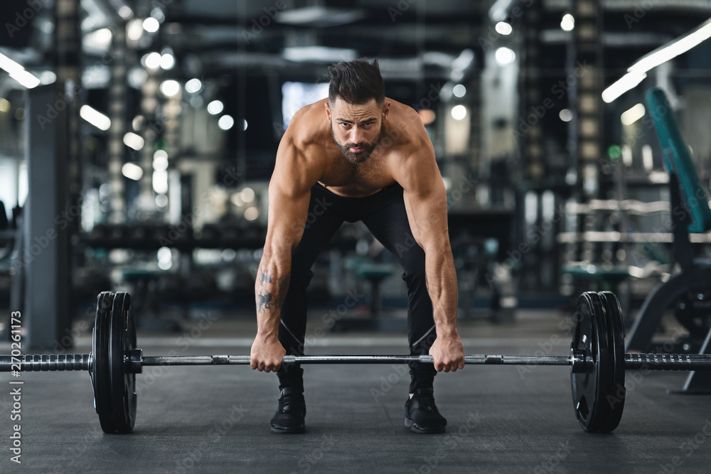 Muscular bodybuilder lifting heavy barbell at gym interior Muscular bodybuilder lifting heavy barbell at gym interior