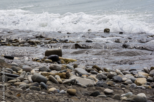 pebble stones on the sea beach, the rolling waves of the sea with foam