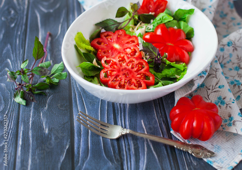 Salad with large ripe red tomato with basil on a wooden table, tomato variety.