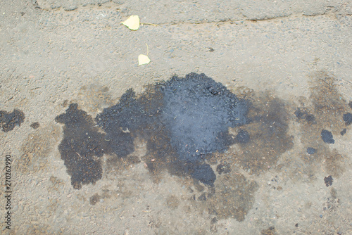 Oil stains on the asphalt. Dirty surface of grey asphalt road. Black oil stains on the sidewalk.