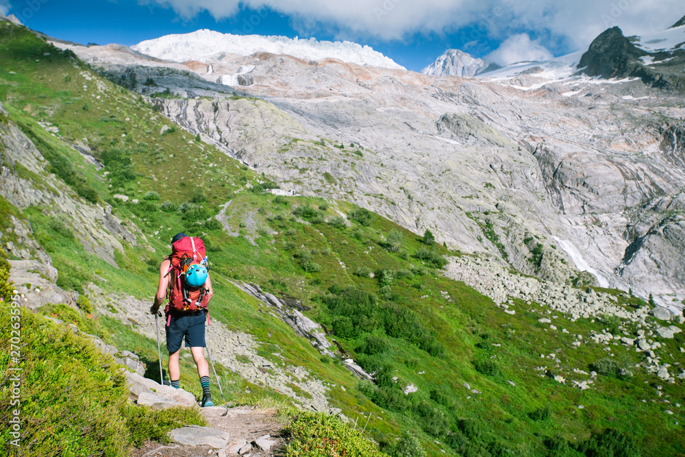 A hiker walking along a steep path in the mountais towards a glacier and high peaks.