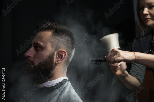 Professional hairdresser barber using talcum powder for his client hair sitting in a barber chair on black background