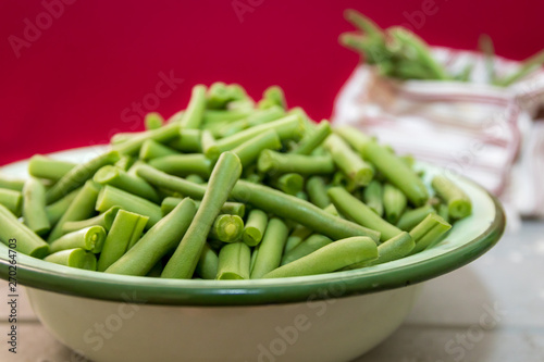 Fresh organic green beans in an antique enamel bowl on a red background