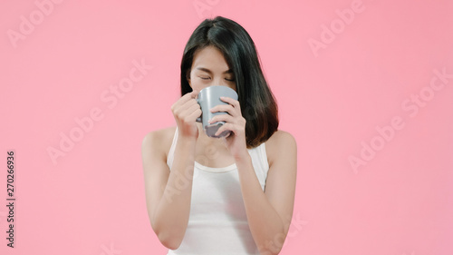 Laughing beautiful Asian woman drinking coffee of tea in casual clothing over pink background studio shot. Happy smiling adorable glad woman rejoices success.