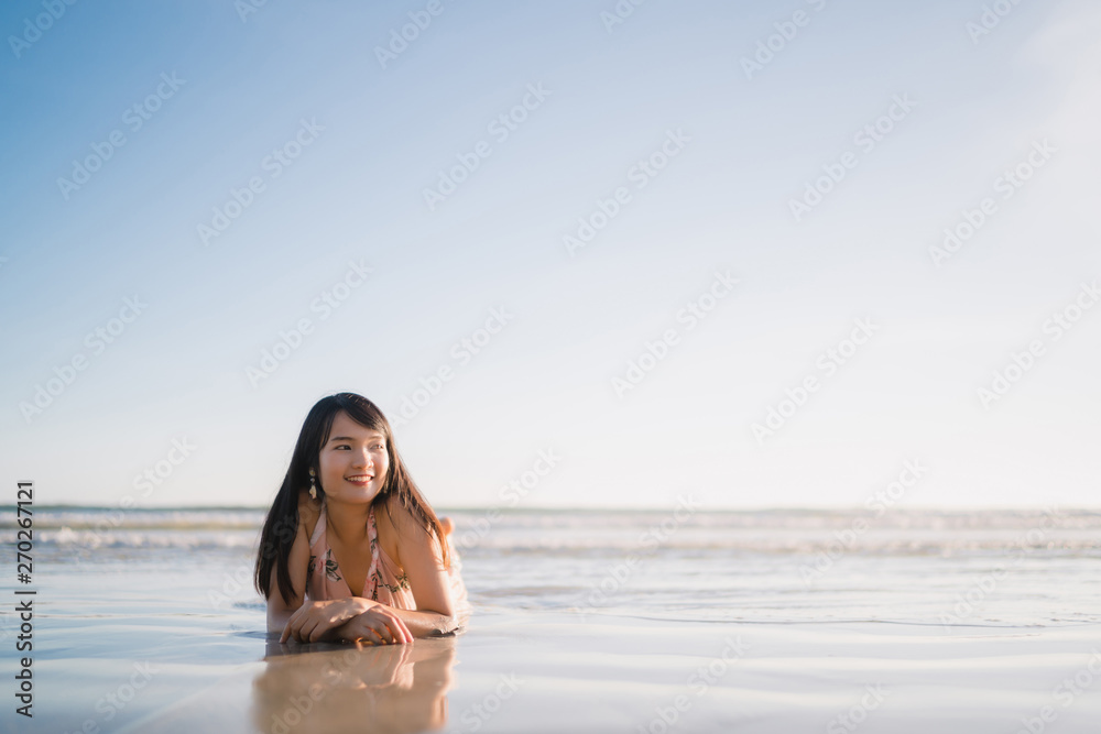 Obraz premium Young Asian woman feeling happy on beach, beautiful female happy relax smiling fun on beach near sea when sunset in evening. Lifestyle women travel on beach concept.