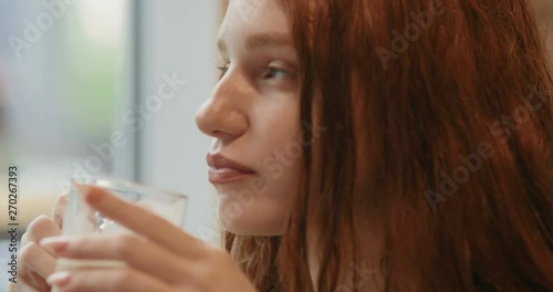 Close-up face of red-haired girl drinking coffee with milk sitting in a cafe. in slow motion. Shot on Canon 1DX mark2 4K camera