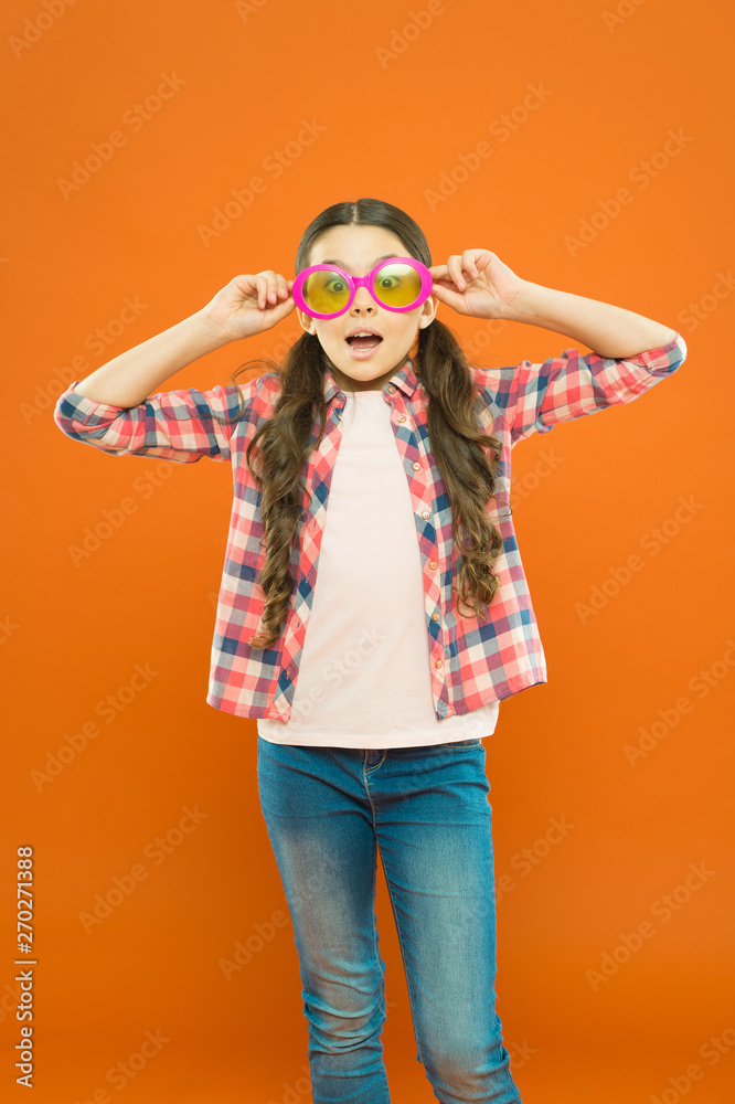 Aint it funny. Little girl looking through funny glasses with color filter on orange background. Funny child wearing sunglasses on surprised face. My eyes go funny