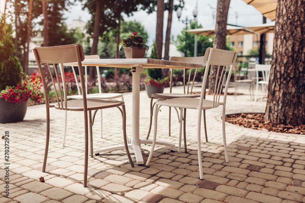 Obraz premium Outdoor cafe in summer park. Empty tables and chairs surrounded with trees and flowers