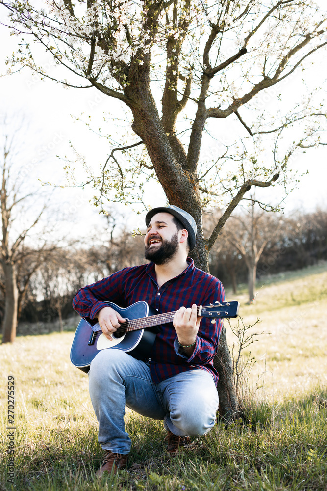 Man playing guitar at a tree on a meadow Man playing guitar at a tree on a meadow