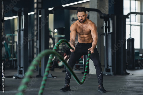 Fitness man working out with battle ropes at gym