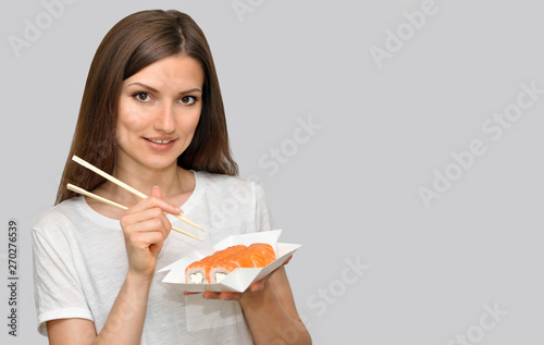 A beautiful young woman in a white T-shirt is smiling and holding a box of rolls of food delivery.