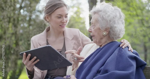 woman and senior grandmother using tablet device for video call at park.Granddaughter and grandma talking together with mobile.Active, caring,loving people relationship.slow motion video photo