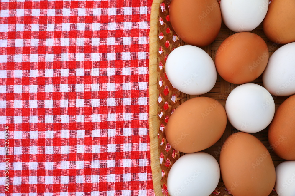 A basket of white and brown eggs on a red-and-white tablecloth, top view A basket of white and brown eggs on a red-and-white tablecloth, top view