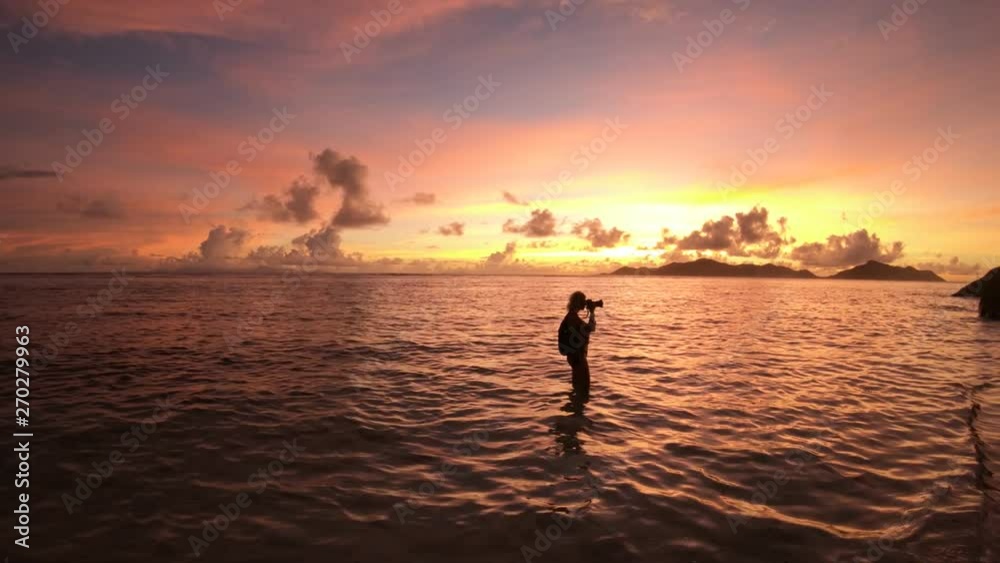 Woman photographer with camera at sunset in Anse Source d'Argent, La Digue, Seychelles. Shallow waters, white pristine sand and turquoise sea. Summer holiday tropical travel. Horizont background. Woman photographer with camera at sunset in Anse Source d'Argent, La Digue, Seychelles. Shallow waters, white pristine sand and turquoise sea. Summer holiday tropical travel. Horizont background.
