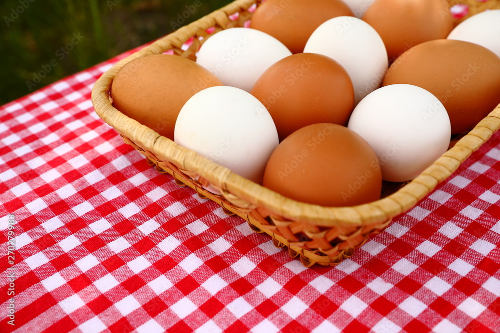 A basket of white and brown eggs on a red-and-white checkd tablecloth, diagonal, blurred green natural background A basket of white and brown eggs on a red-and-white checkd tablecloth, diagonal, blurred green natural background