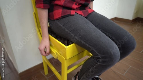 close-up of a girl in a red-black klechaty shirt and jeans sitting on a bright yellow chair studded with sharp nails