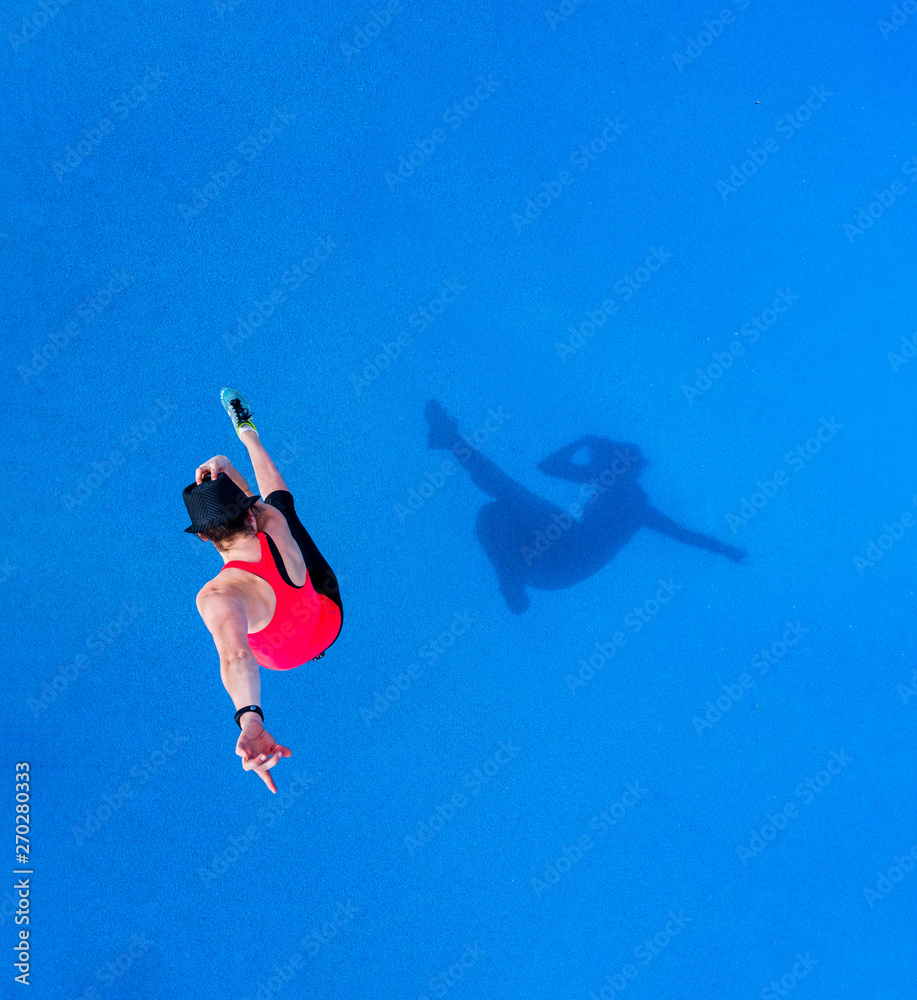 Jumping young woman and her shadow on blue background, top view