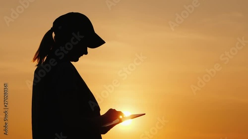 Silhouette of a woman farmer working with a tablet at sunset photo