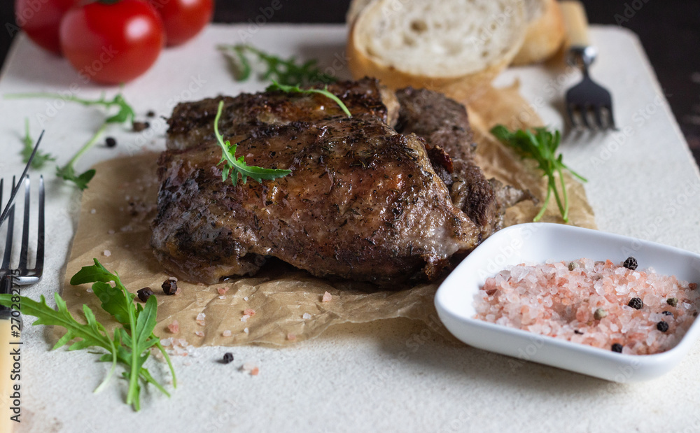 Roast beef with herbs and spices served with arugula, tomatoes and fresh bread on baking stone. Top view.