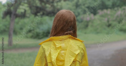 Attractive red-haired young woman in a yellow rain coat walking in the forest. The girl laughs and rejoices in the spring warm rain. tracking shot. in slow motion. Shot on Canon 1DX mark2 4K camera photo