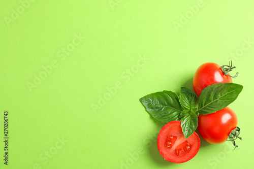 Fresh cherry tomatoes with basil on color background, space for text. Ripe vegetables
