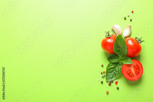 Fresh cherry tomatoes with basil, pepper and garlic on color background, space for text. Ripe vegetables