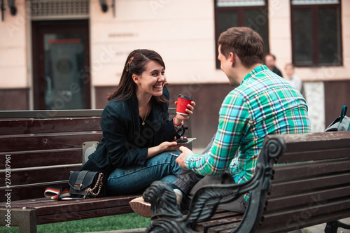 smiling couple sitting on bench talking to each other drinking coffee