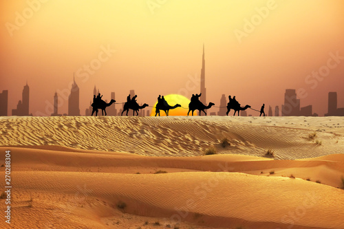 Dubai skyline at horizon with camel ride caravan silhouette in desert