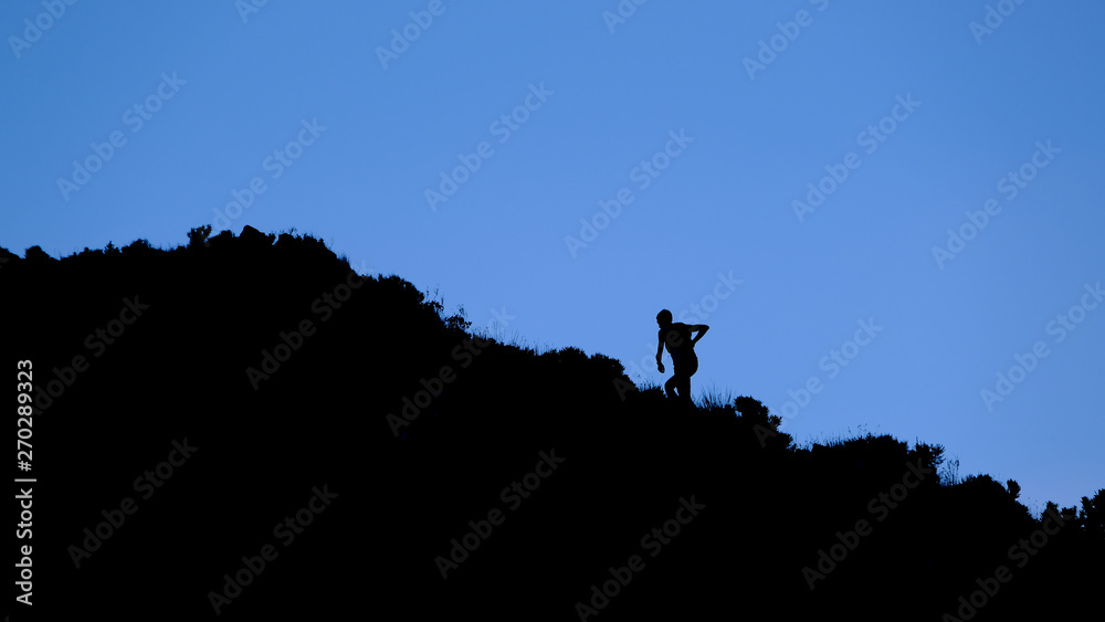 Dramatic silhouette of a person hiking and climbing a steep mountain