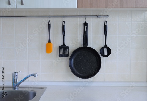 Frying pan with non-stick coating, a spatula for a steak, a spoon against the background of a tiled wall. The interior of the kitchen.