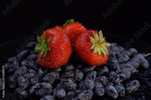 Dark honeysuckle berries and sweet strawberries against black background  space for text. Concept of healthy and proper nutrition.