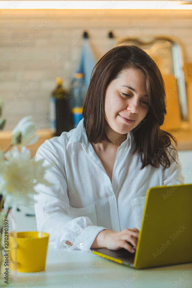 young pretty caucasian woman talking on the phone sitting in front of laptop in the kitchen young pretty caucasian woman talking on the phone sitting in front of laptop in the kitchen