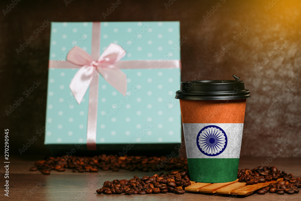 Paper cup for coffee with the image of the Indian flag. Grains lie on a wooden surface.