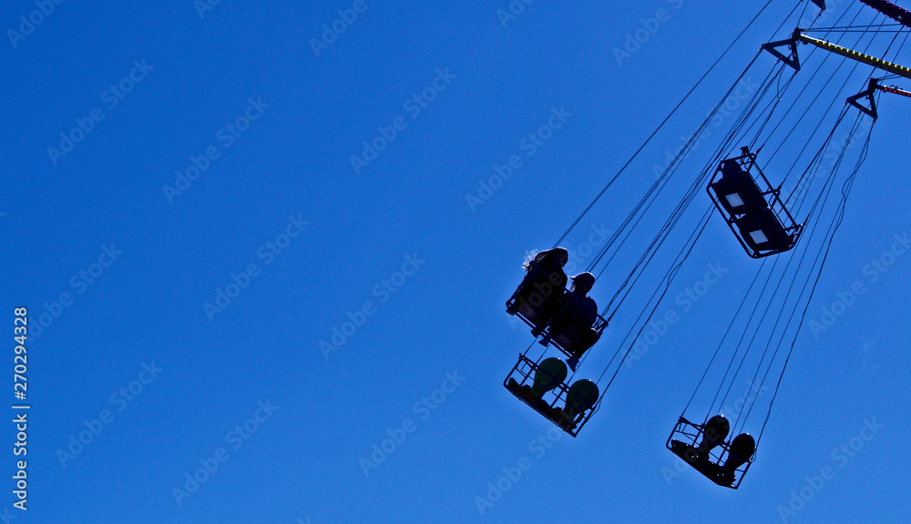 Fairground ride, flying chairs, bright blue sky silhouette Fairground ride, flying chairs, bright blue sky silhouette