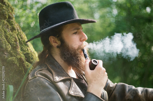 Film photo. Portrait of bearded man in hat smoking tobacco pipe.