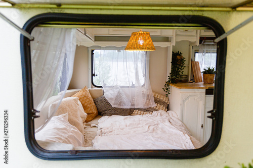 Wallpaper Mural View through the window into the interior of the camper van. Unmade bed, pillows, white wooden interior with lamp center. Cozy sleeping place for a young couple to sleep inside a camper for traveling Torontodigital.ca