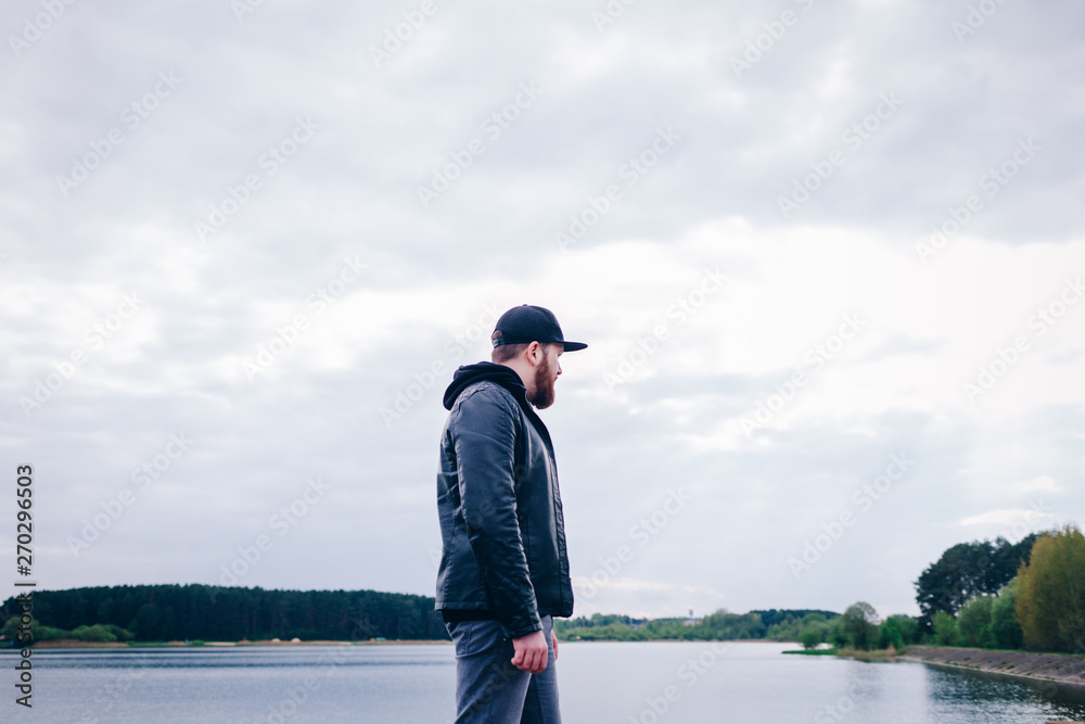 a lonely man in a leather jacket near the river stands and looks into the distance